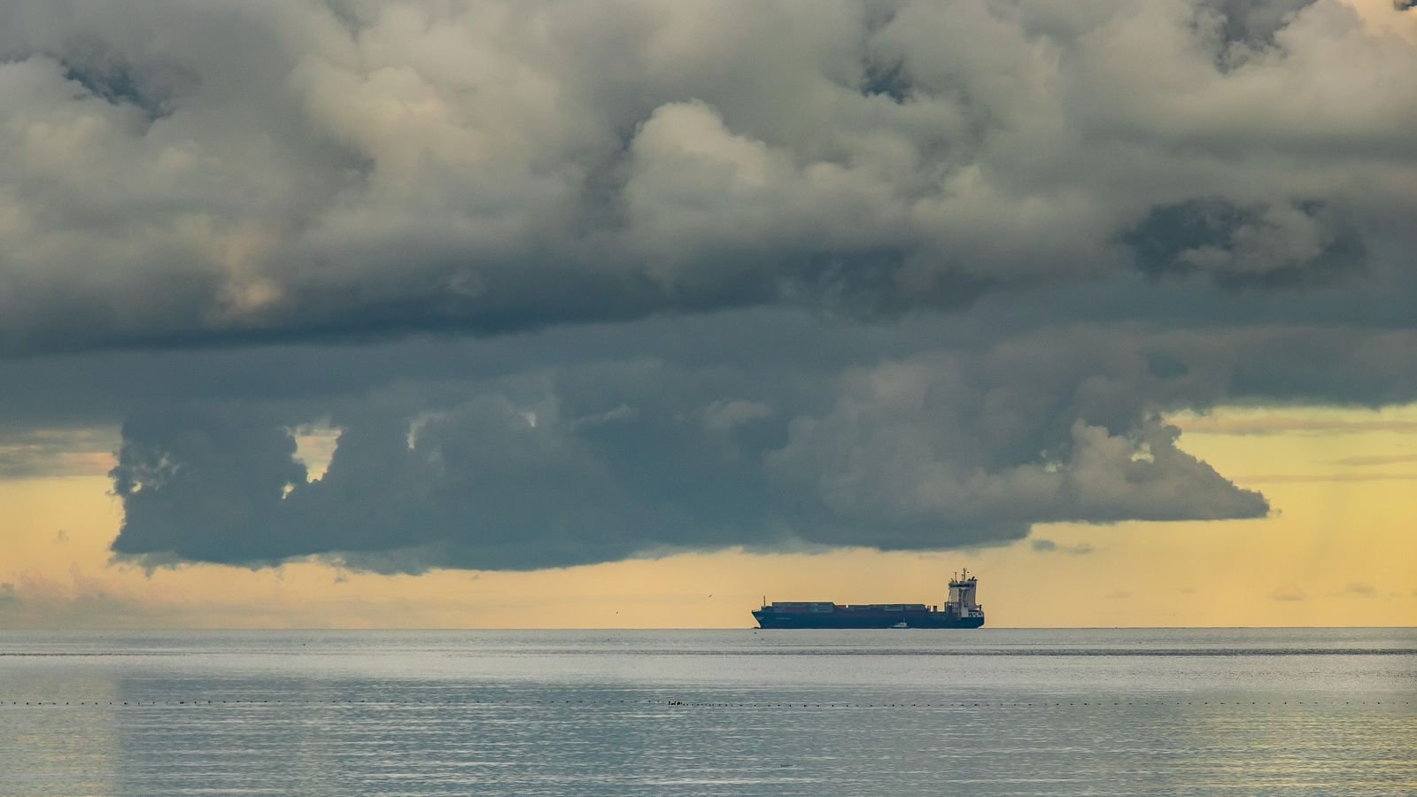 A solitary oil tanker sailing under dramatic clouds on the horizon, representing the Strait of Hormuz oil supply tensions